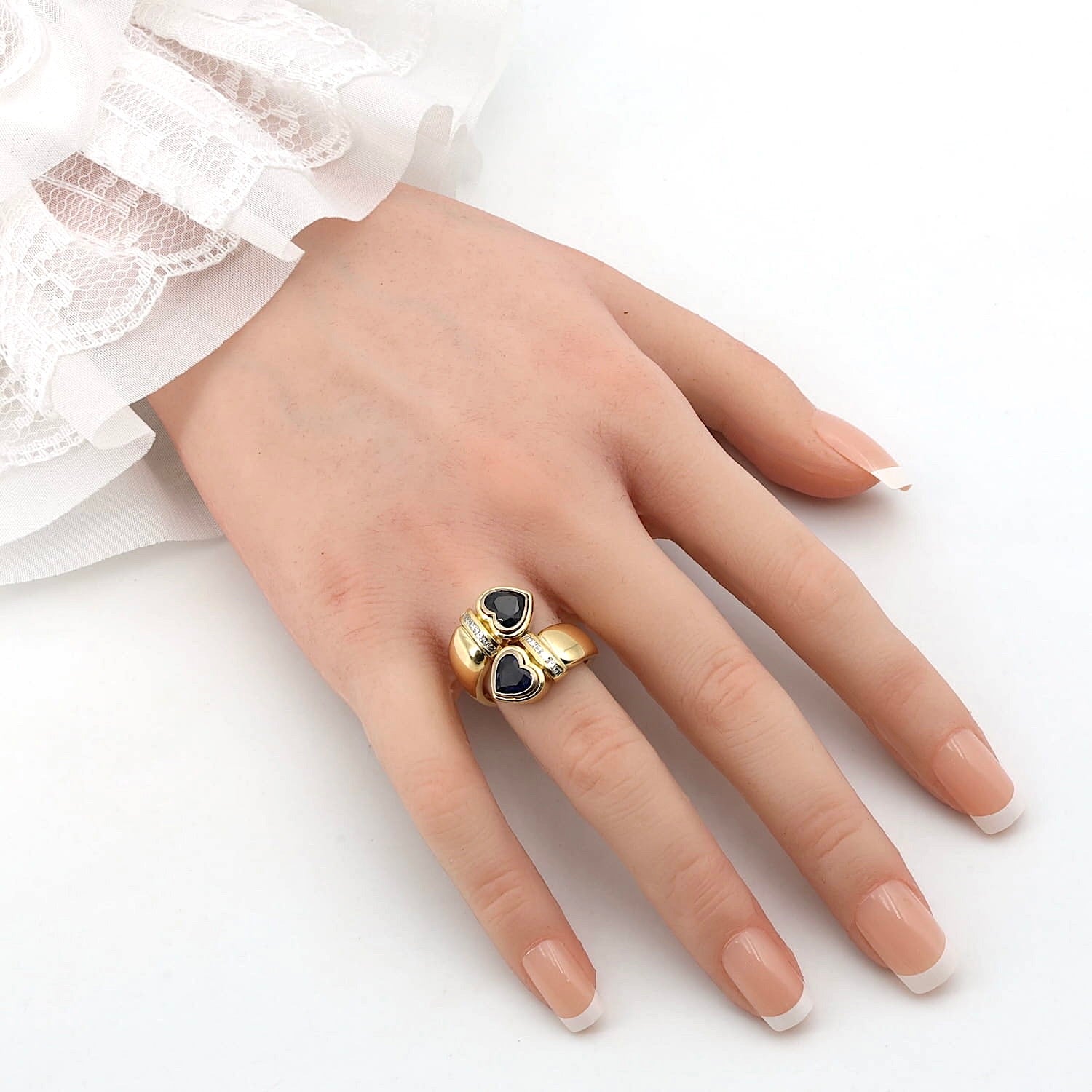 Ring in 750er Gelbgold mit zwei blauen Saphiren in Herzform und Diamanten, an einer künstlichen Hand