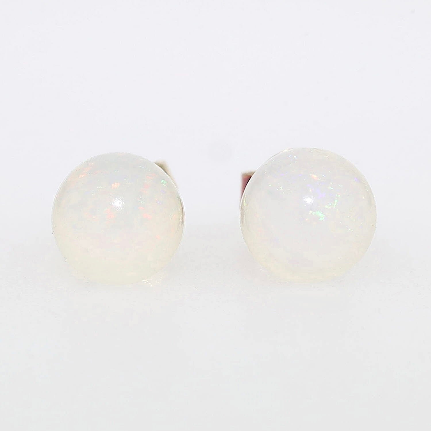 Pair of stud earrings in 585 yellow gold, each with a white opal ball, lying frontally on a gray background