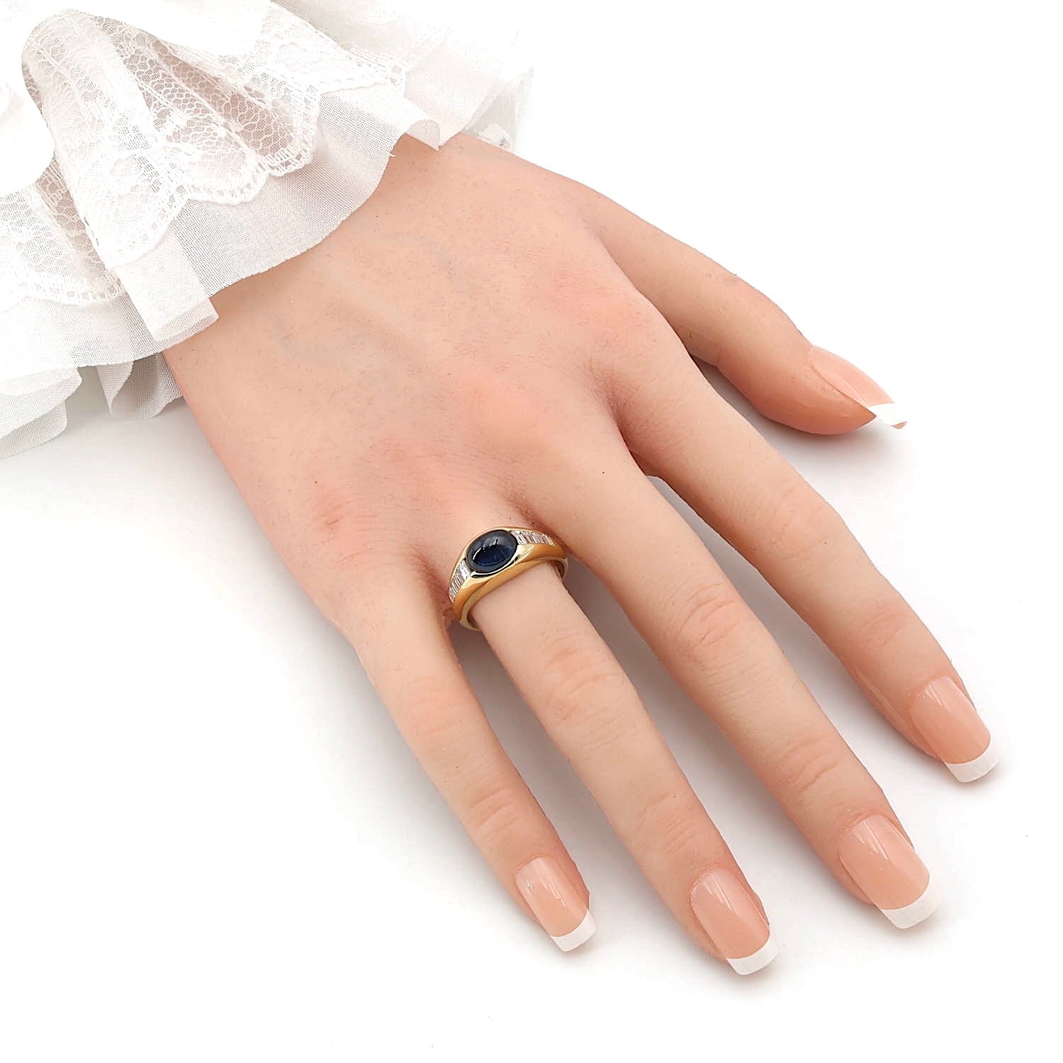 Ring in 750er Gelbgold mit einem blauen Saphir-Cabochon und Diamanten, an einer künstliche Hand