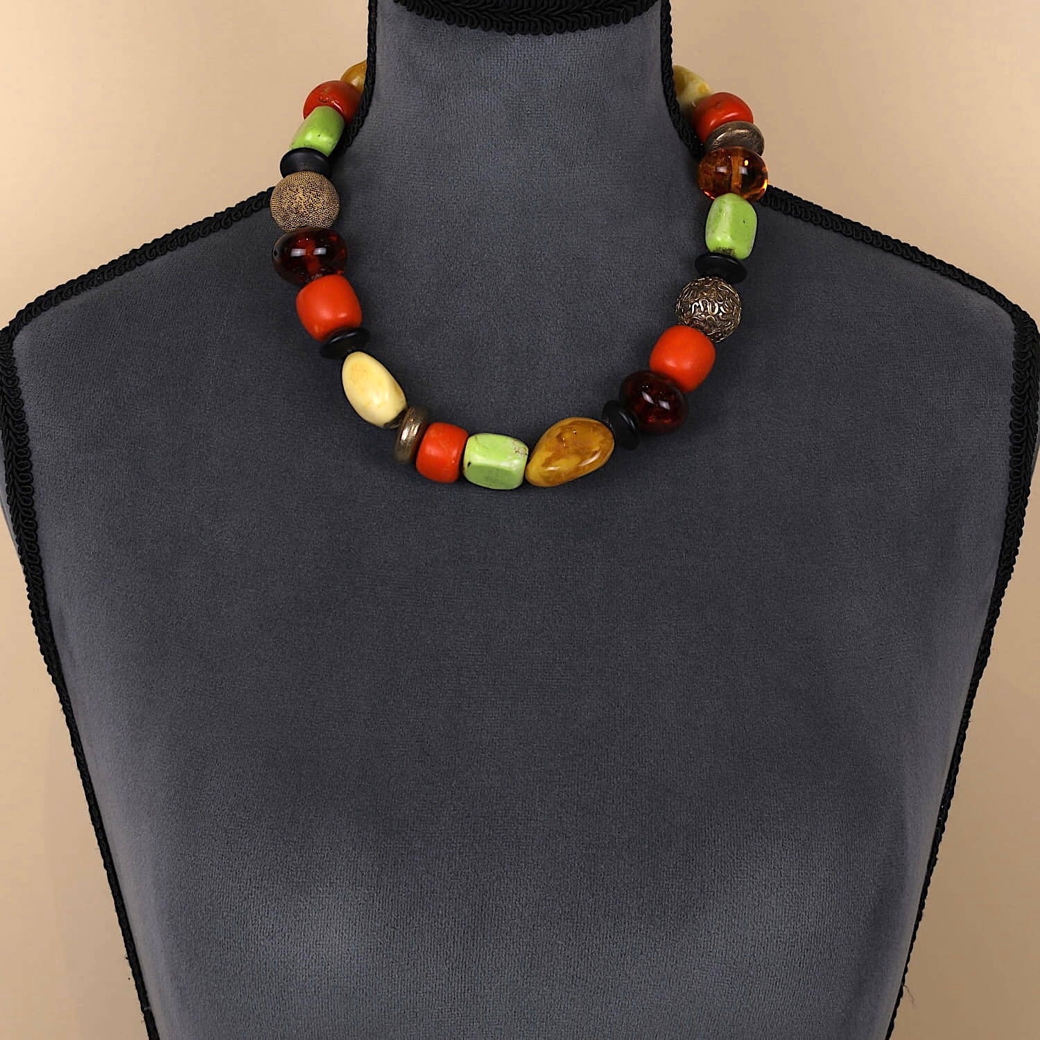 Designerkette mit Bernstein, Koralle, Magnesit und vergoldeten Silberelementen, an einer dunklen Büste