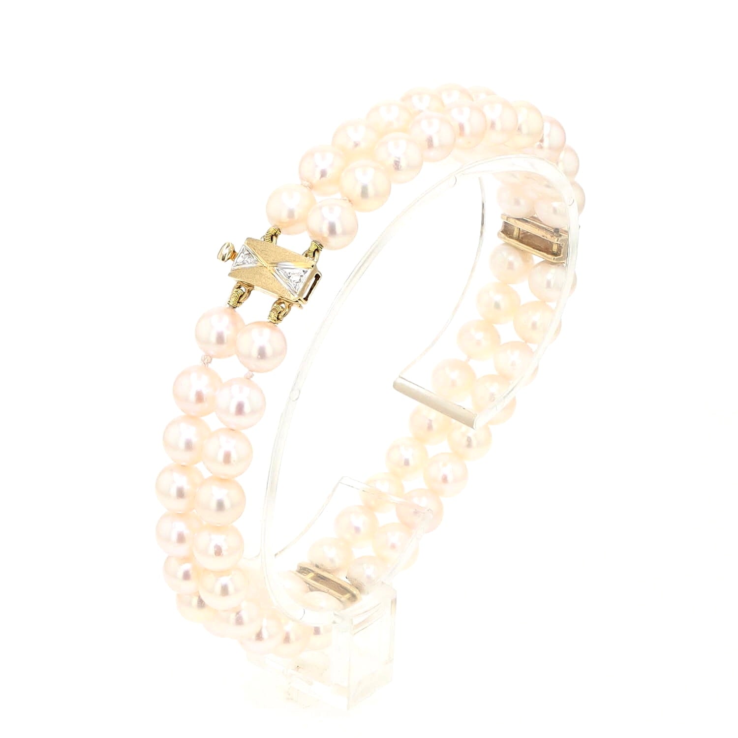 Akoya-Zuchtperlenarmband in zwei Reihen mit einem Schloss und Goldelementen aus 585er Gelbgold mit Diamanten, stehend auf einem Halter aus Kunststoffleicht links gedreht